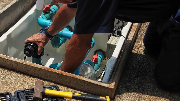 Técnico instalando conexões de água numa caixa no chão, com as ferramentas ao lado